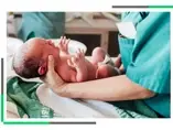 Noworodek trzymany przez położną tuż po porodzie.