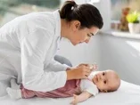 Pediatra w białym fartuchu bada niemowlę leżące na stole w gabinecie lekarskim				