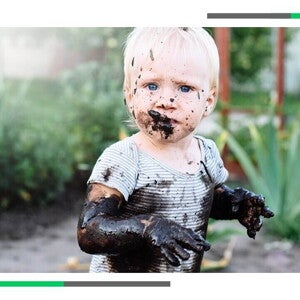 Dziecko ubrudzone błotem siedzące w ogrodzie