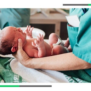 Noworodek trzymany przez położną tuż po porodzie.