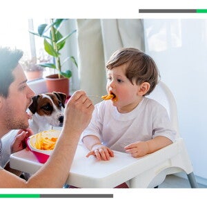 Opiekun karmi małe dziecko z łyżeczki pod czujną obserwacją ich psa