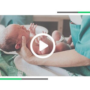 Noworodek trzymany przez położną tuż po porodzie.