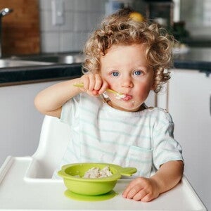 Mały chłopiec siedzący na wysokim krześle i samodzielnie jedzący owsiankę łyżką