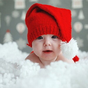 dziecko w czerwonej czapeczce leżące w chmurze śniegu