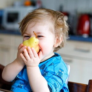 małe dziecko je gruszkę i się uśmiecha