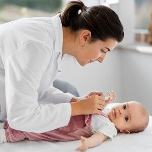 Pediatra w białym fartuchu bada niemowlę leżące na stole w gabinecie lekarskim				