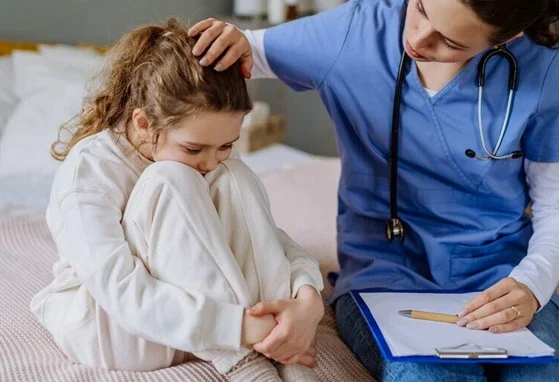 Lekarz siedzi obok małej pacjentki i ją pociesza