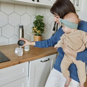 Mama trzymająca dziecko na rękach i przygotowująca mleko modyfikowane