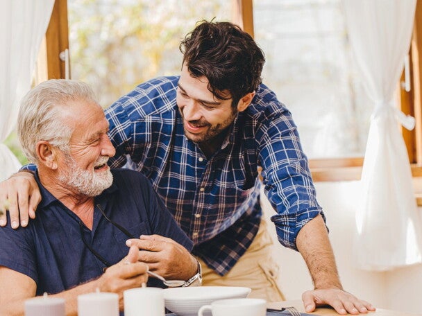 Opiekun pomaga starszemu mężczyźnie podczas posiłku, wspierając żywienie seniora w warunkach domowych.