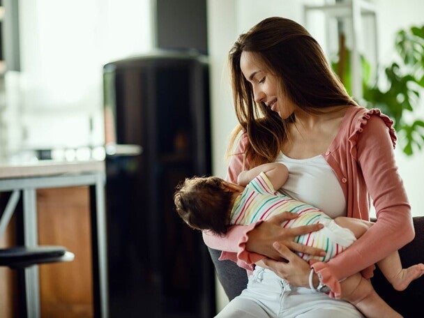małe dziecko karmione piersią na rękach mamy w domu