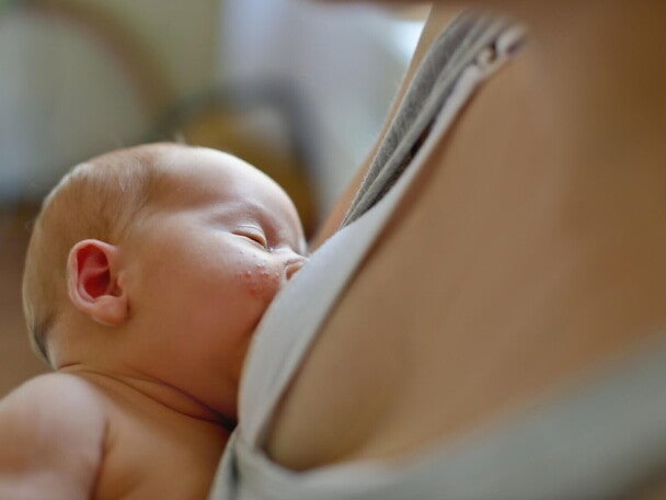 dziecko karmione piersią na rękach mamy z wysypką na policzku