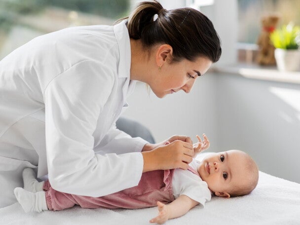 Pediatra w białym fartuchu bada niemowlę leżące na stole w gabinecie lekarskim				