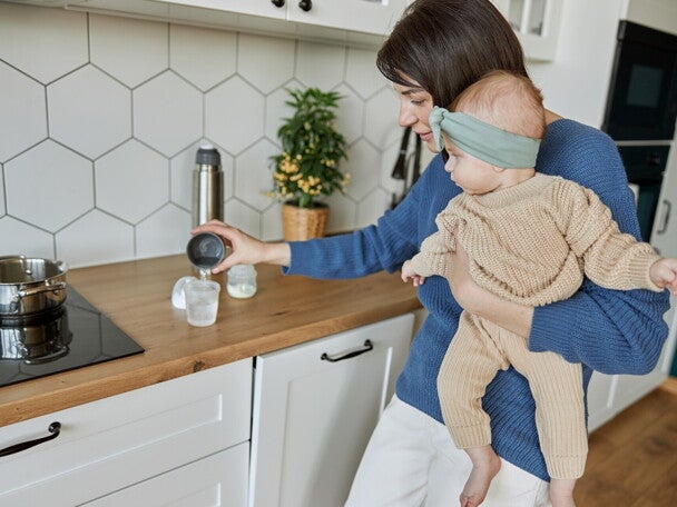 Mama trzymająca dziecko na rękach i przygotowująca mleko modyfikowane