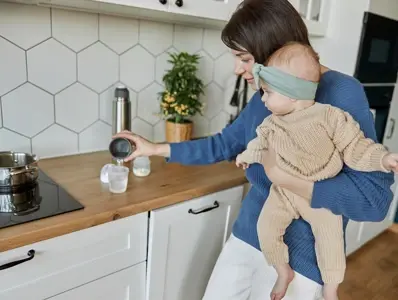 Zmiana mleka modyfikowanego w diecie niemowląt – co warto wiedzieć? Mama trzymająca dziecko na rękach i przygotowująca mleko modyfikowane